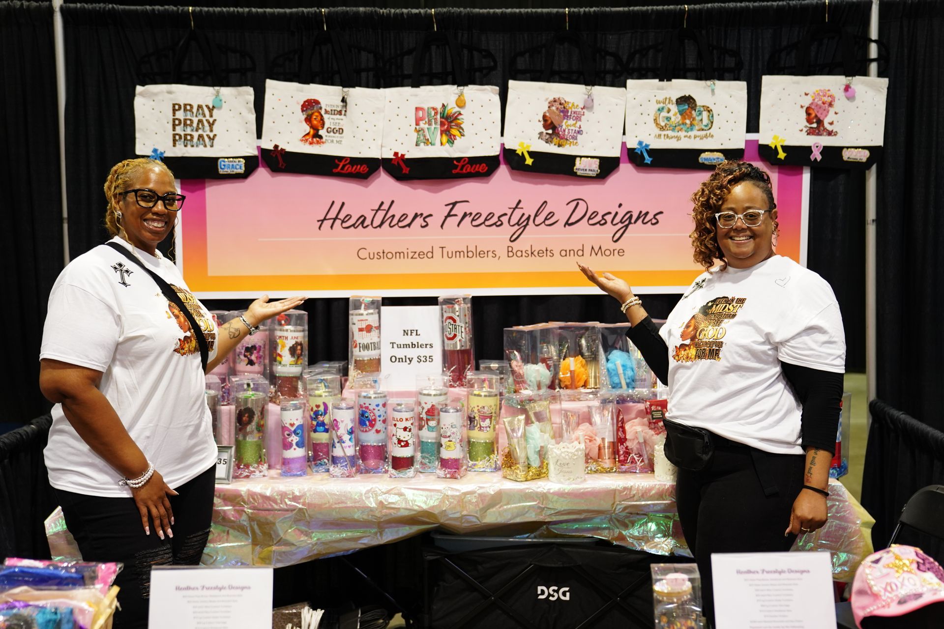 Vendor booth with pink banner and colorful products displayed, with two people standing beside the table