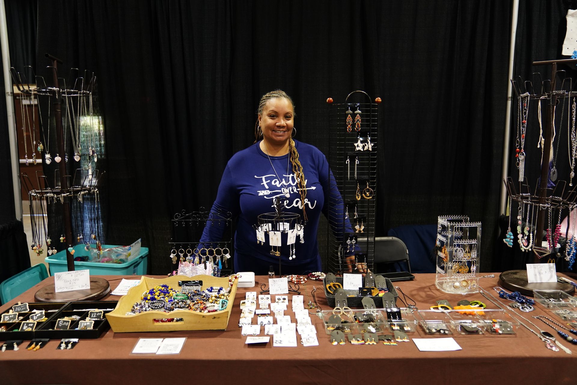 Vendor at a table displaying jewelry and small items at an indoor market booth