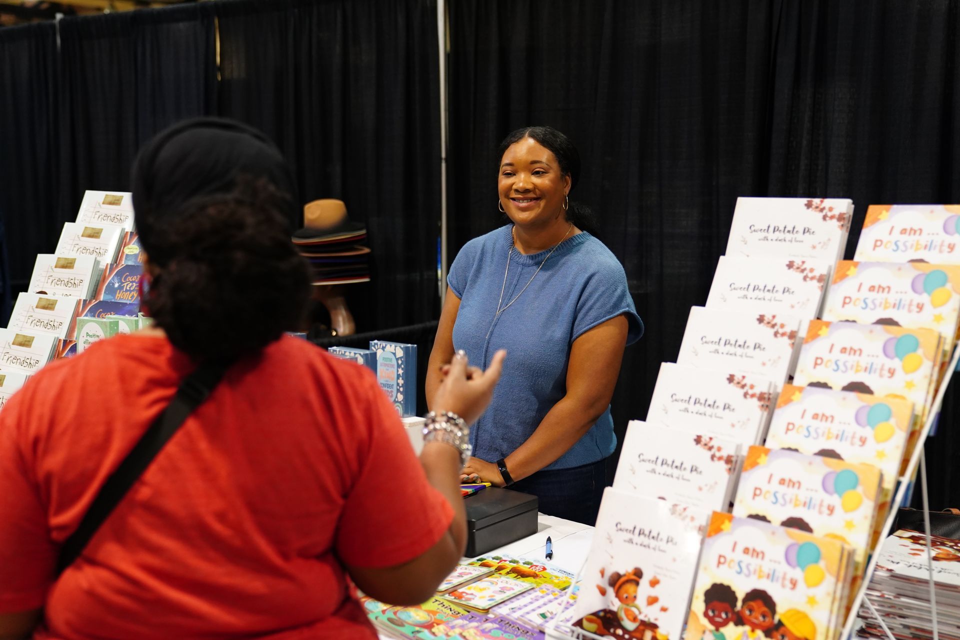 Vendor smiling at a booth with colorful books or brochures displayed on a table