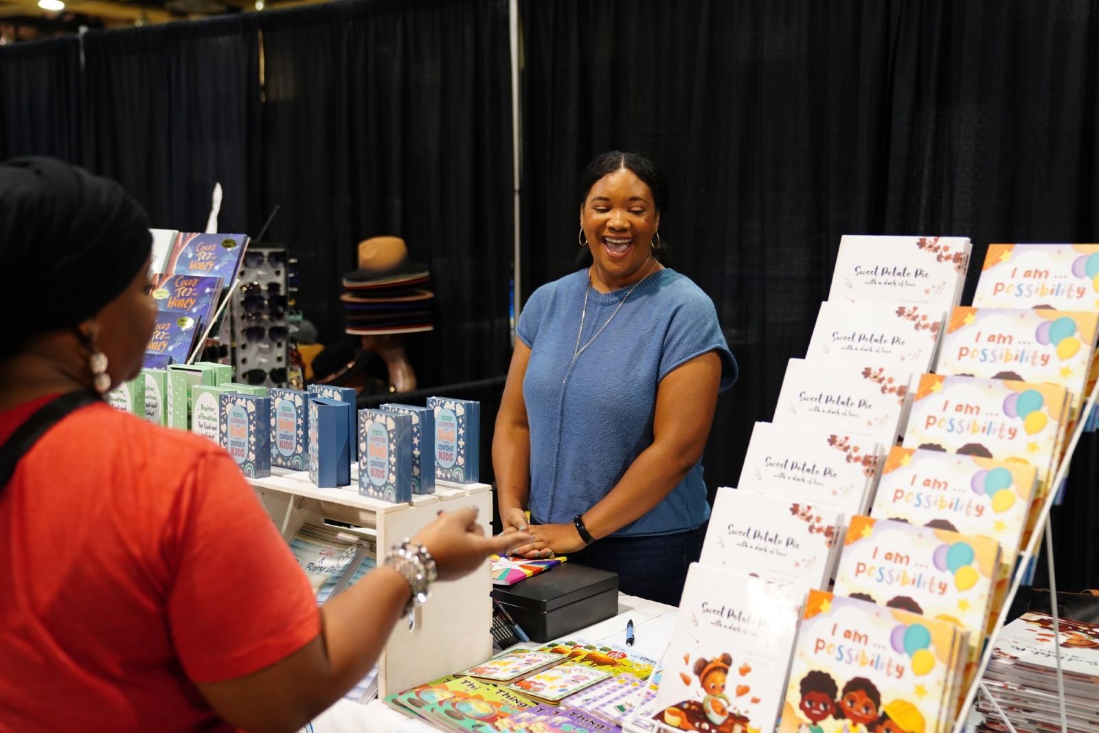 Vendor smiling at a market stall with colorful books and crafts displayed on a table
