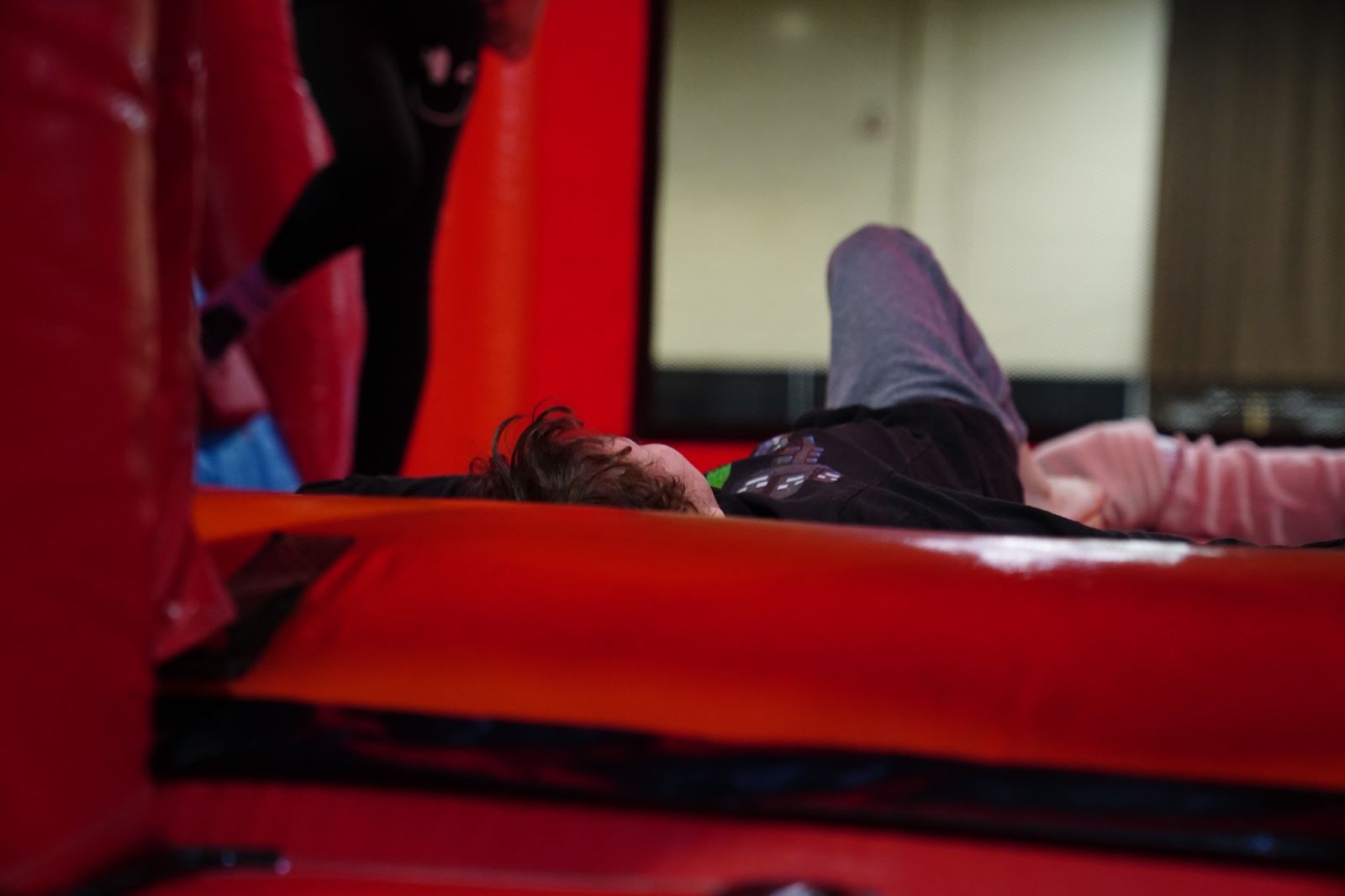 Person lying on a red inflatable mattress in an indoor play area