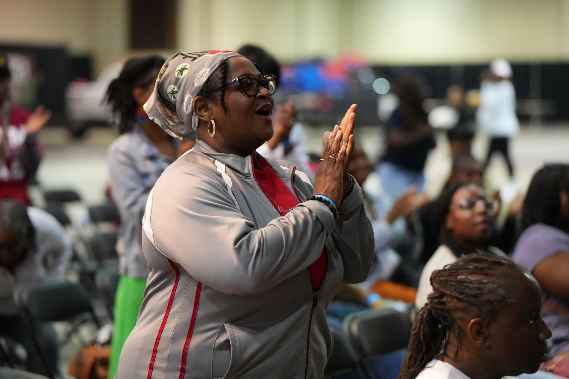 Woman in a gray jacket claps during a seated indoor event.