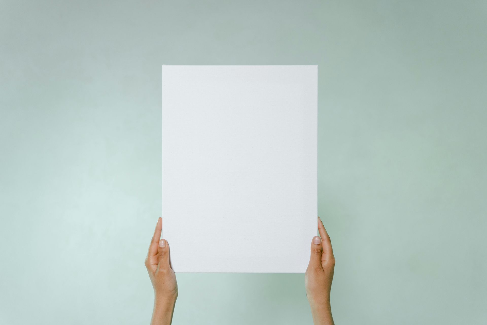 Hands holding a blank white sheet of paper against a light green background
