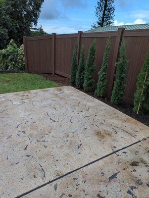 A concrete driveway with a wooden fence and trees in the background.