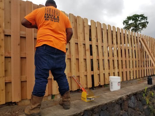 A man in an orange shirt is painting a wooden fence.