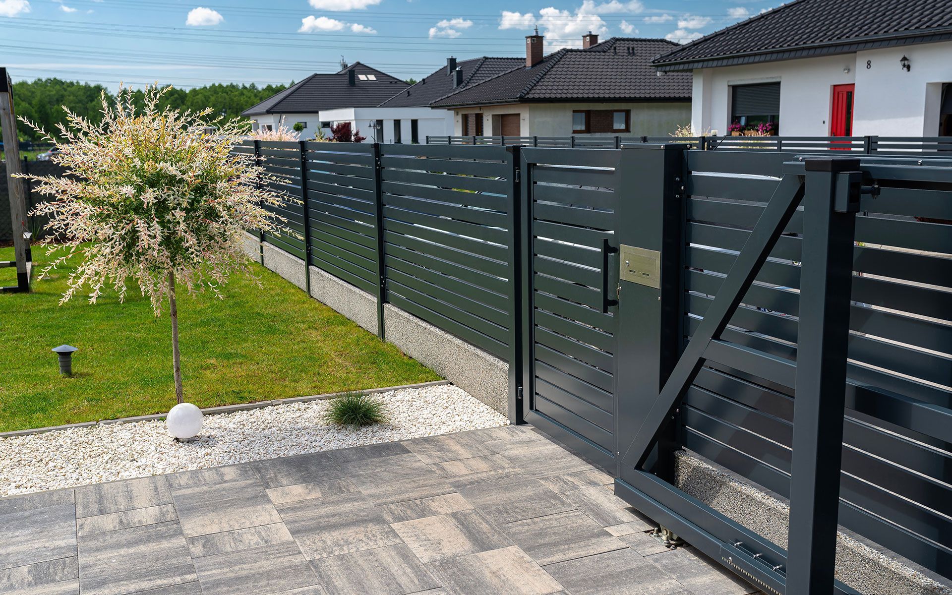 A black fence with a sliding gate in front of a house.