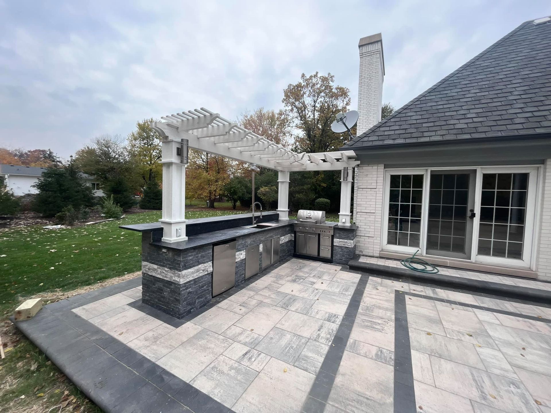 A patio with a kitchen and a pergola in front of a house.