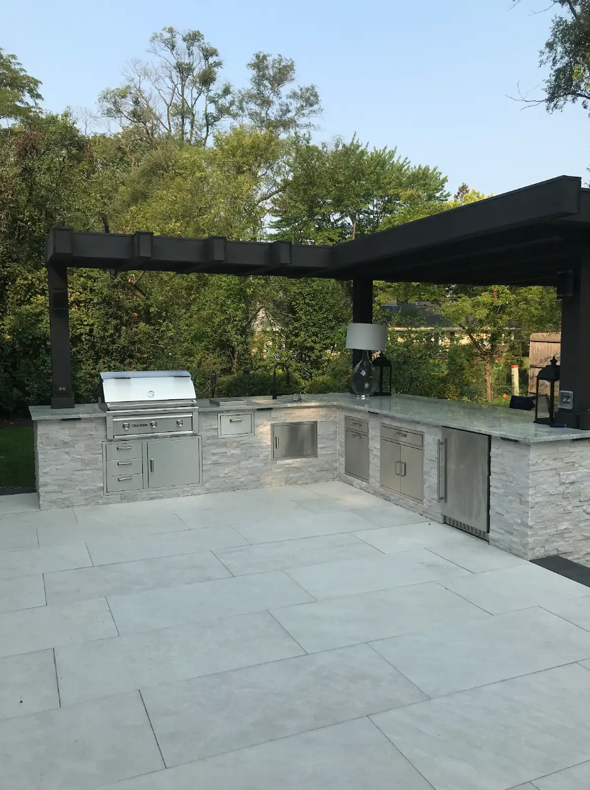 Outdoor kitchen with stainless steel grill, cabinets, and pergola roof.