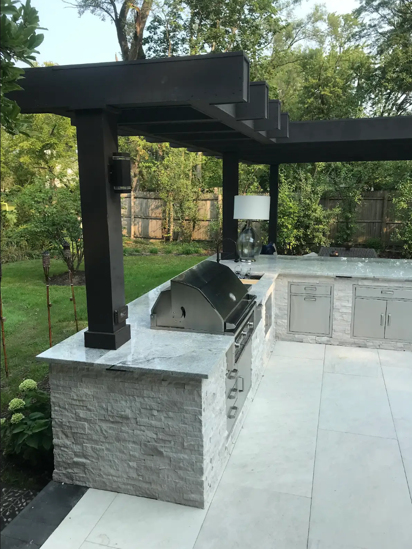 Outdoor kitchen with gray stone facade, stainless steel grill, and dark wood pergola.