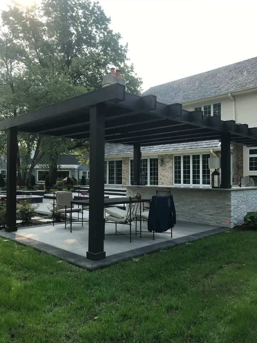 Dark pergola over patio with seating, built-in counter, and grass lawn.