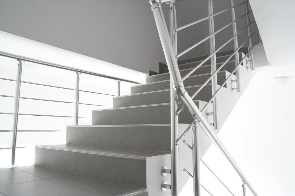 Escalera de hormigón gris con barandillas de acero inoxidable sobre una pared blanca.