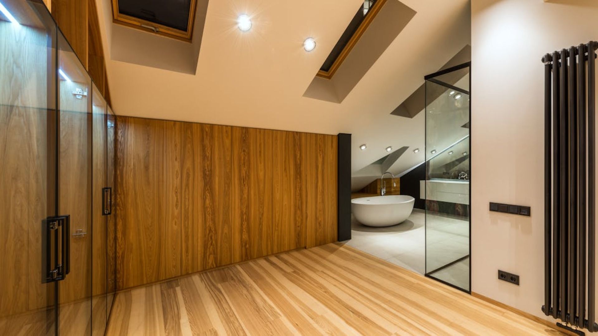 Un baño moderno con paredes y suelos de madera, ducha de cristal, bañera blanca y tragaluz.
