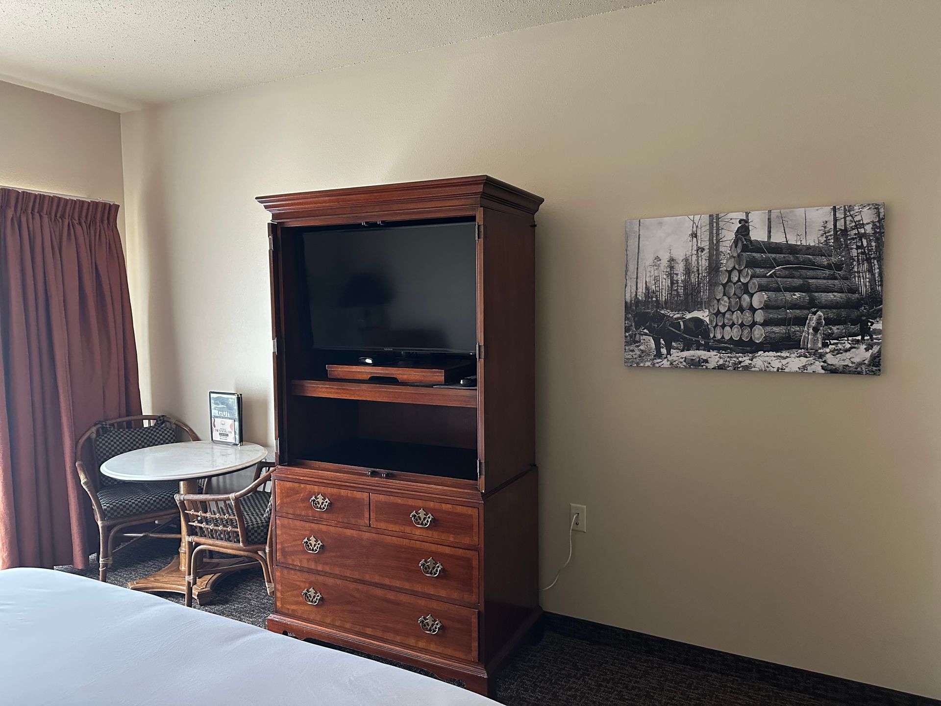 Bedroom with dark wood TV stand, small table and chair, and artwork on a light wall.
