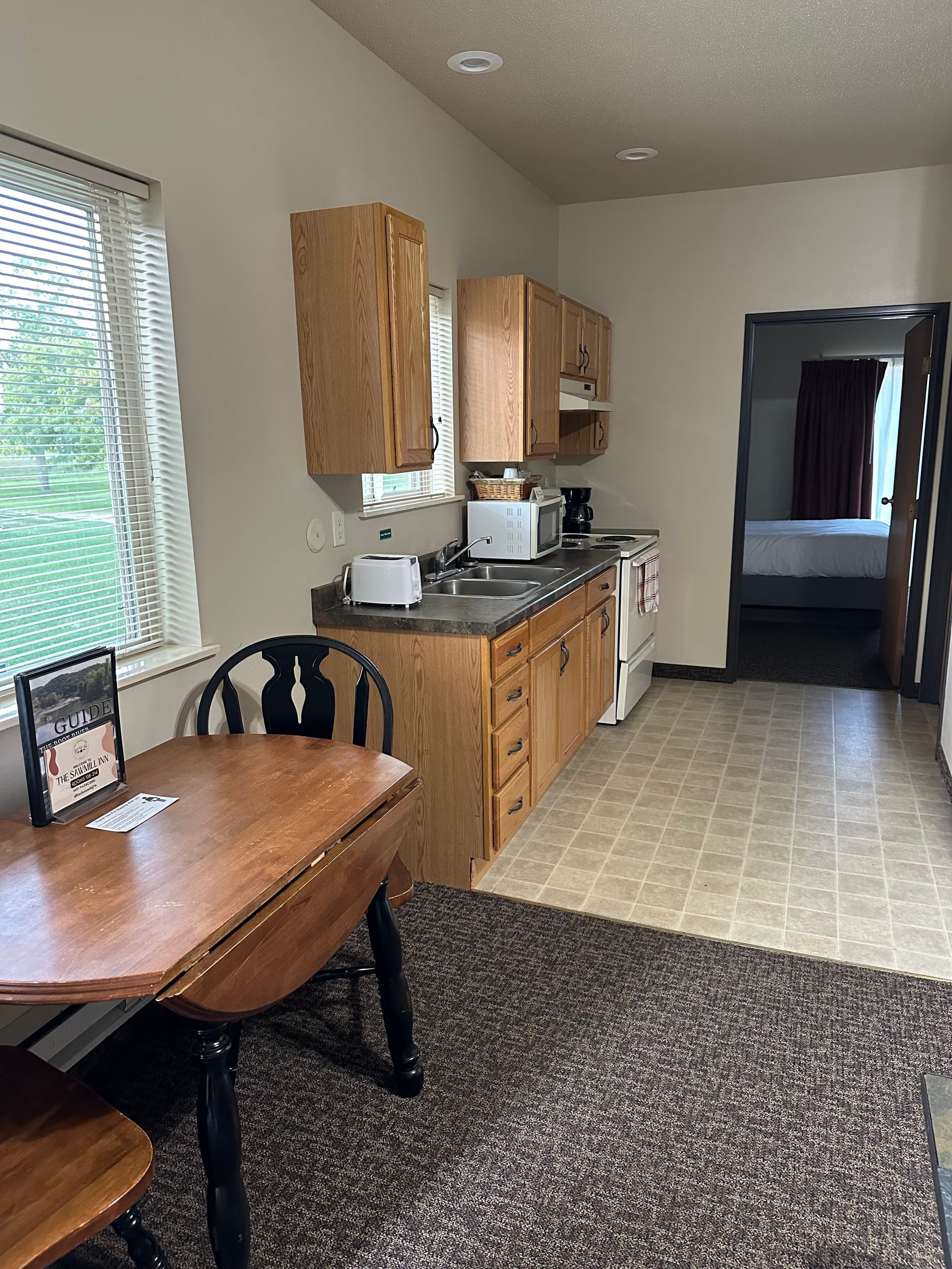 Kitchen with wooden cabinets, small appliances, and a dining table with two chairs. A bedroom is visible in the distance.