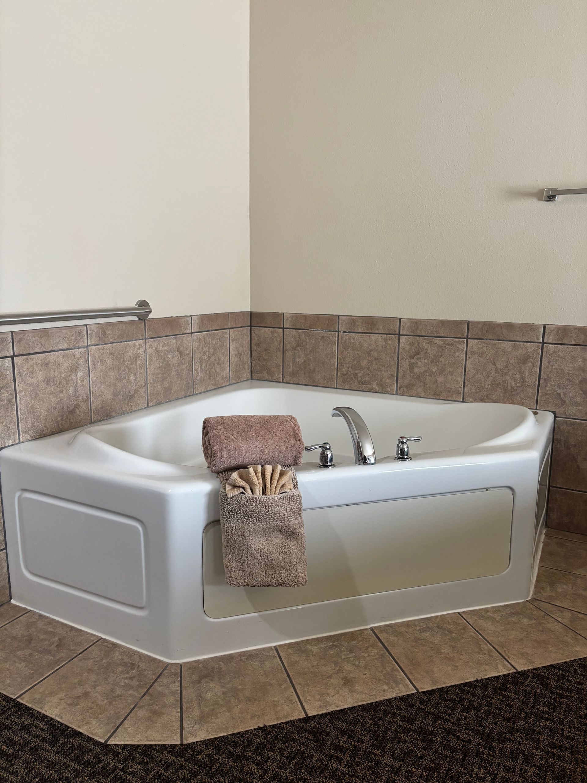 Corner jacuzzi tub with beige towels, surrounded by tile and light walls.