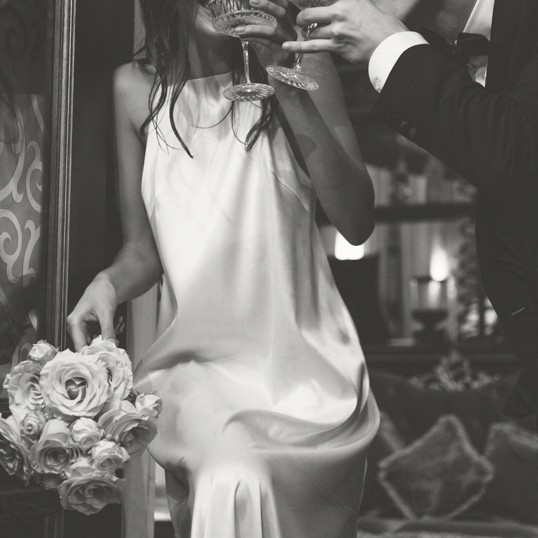 A woman in a white dress is holding a bouquet of flowers and a glass of wine.