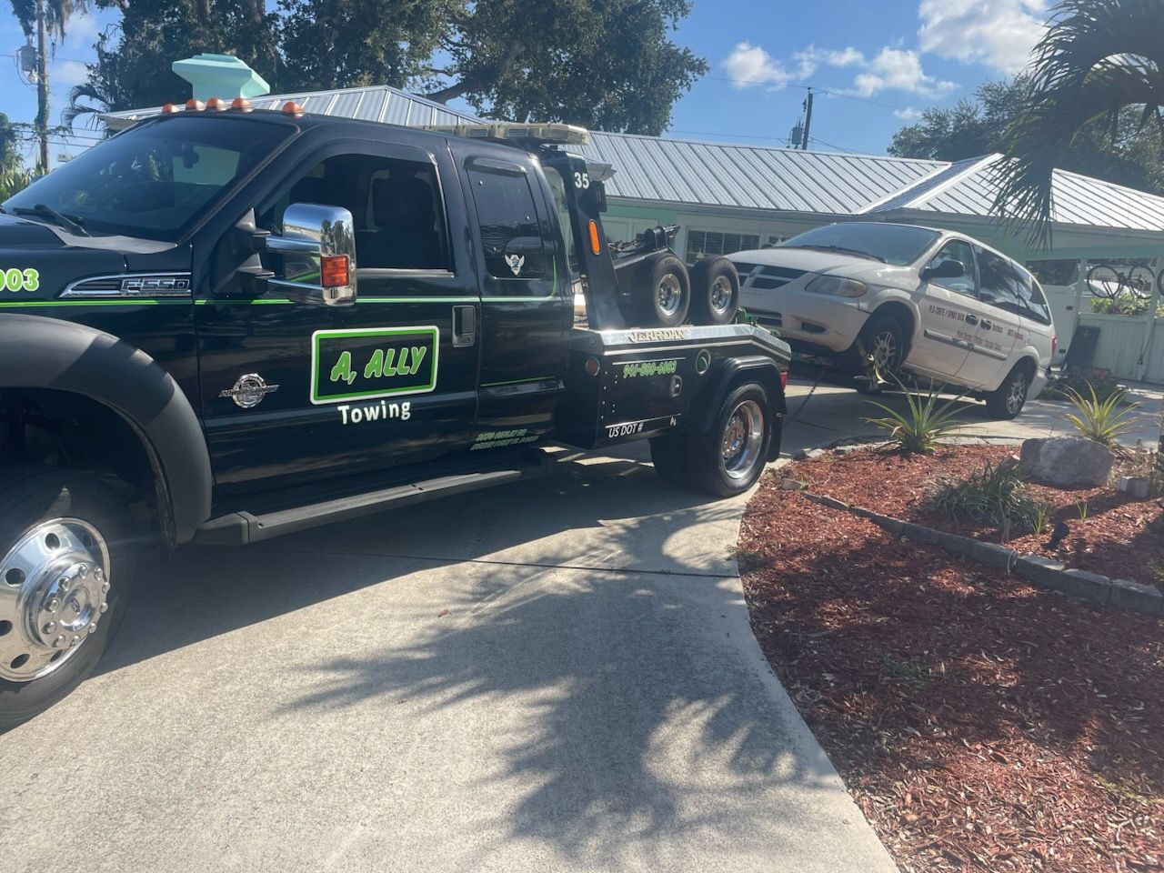 Tow truck operator in orange vest loading a white car onto a flatbed on a roadside