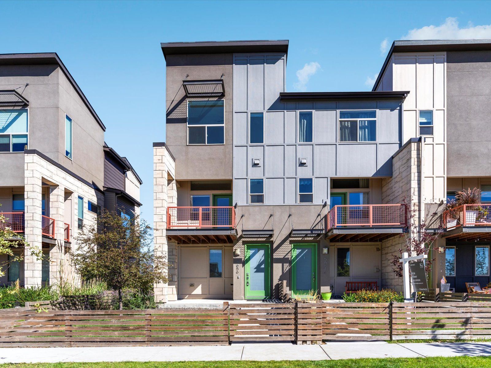 Modern townhouses with gray and tan exteriors, small balconies, and colorful doors.