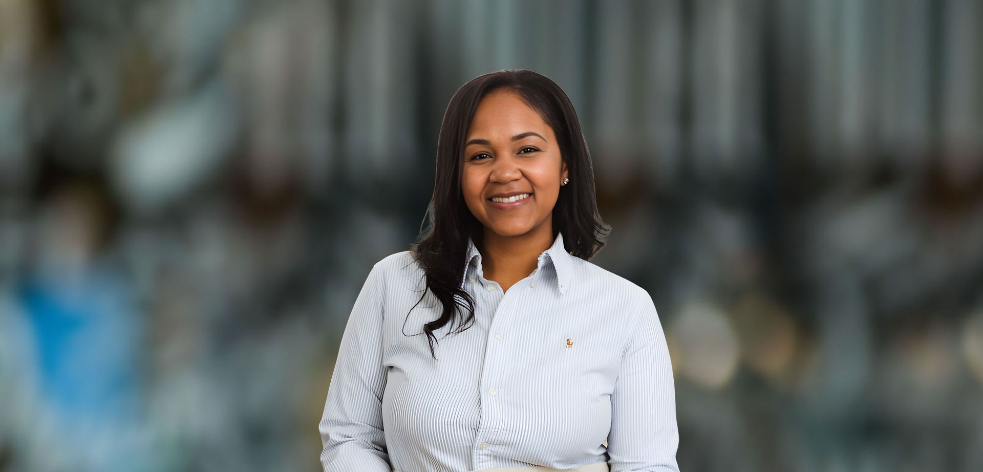 Woman in a blue and white striped shirt smiles at the camera in front of a blurry background.