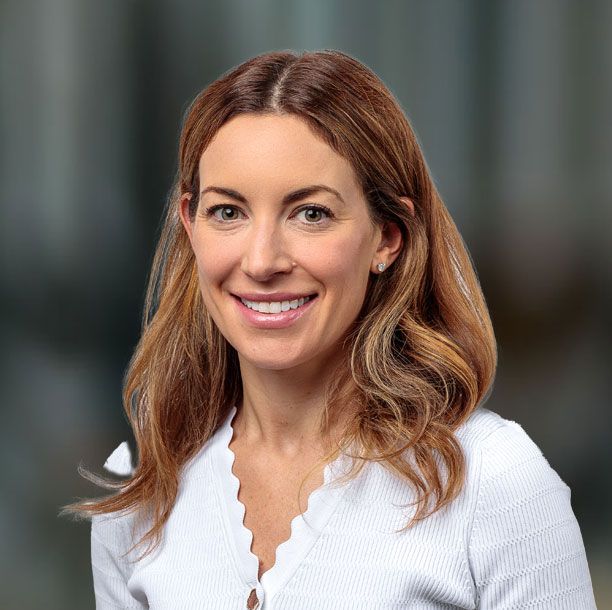 Smiling woman with light brown hair wearing a white sweater, against a blurred background.