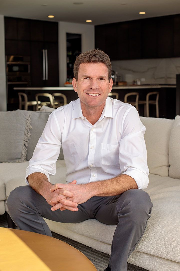 A man in a white shirt is sitting on a couch in a living room.