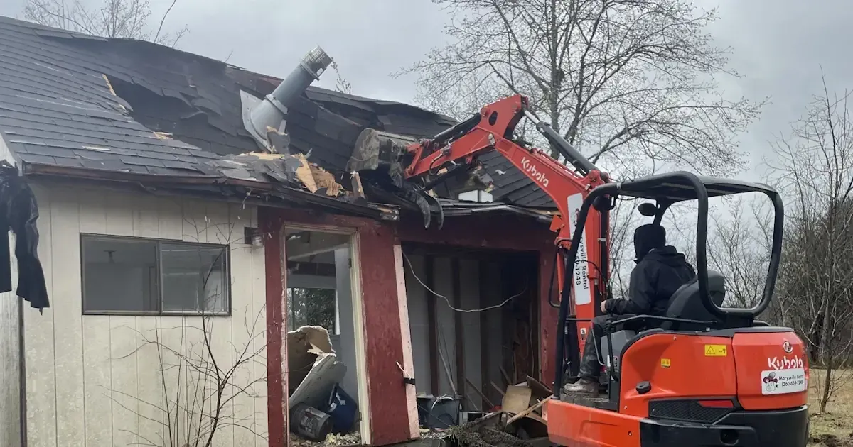 A man is driving an excavator to demolish a house.