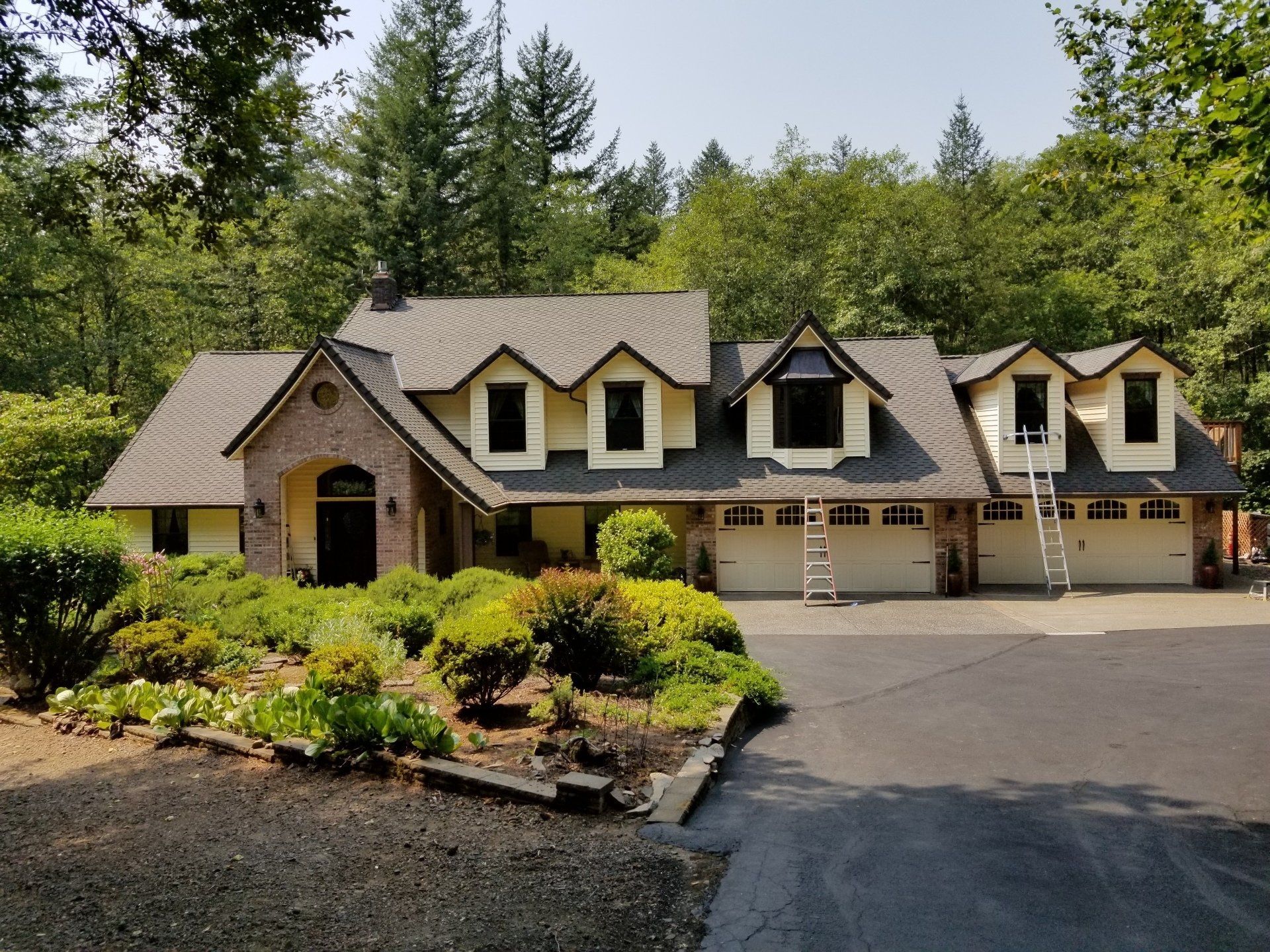 Beige house with dark roof, three dormers, brick entrance, three-car garage, and manicured landscaping.