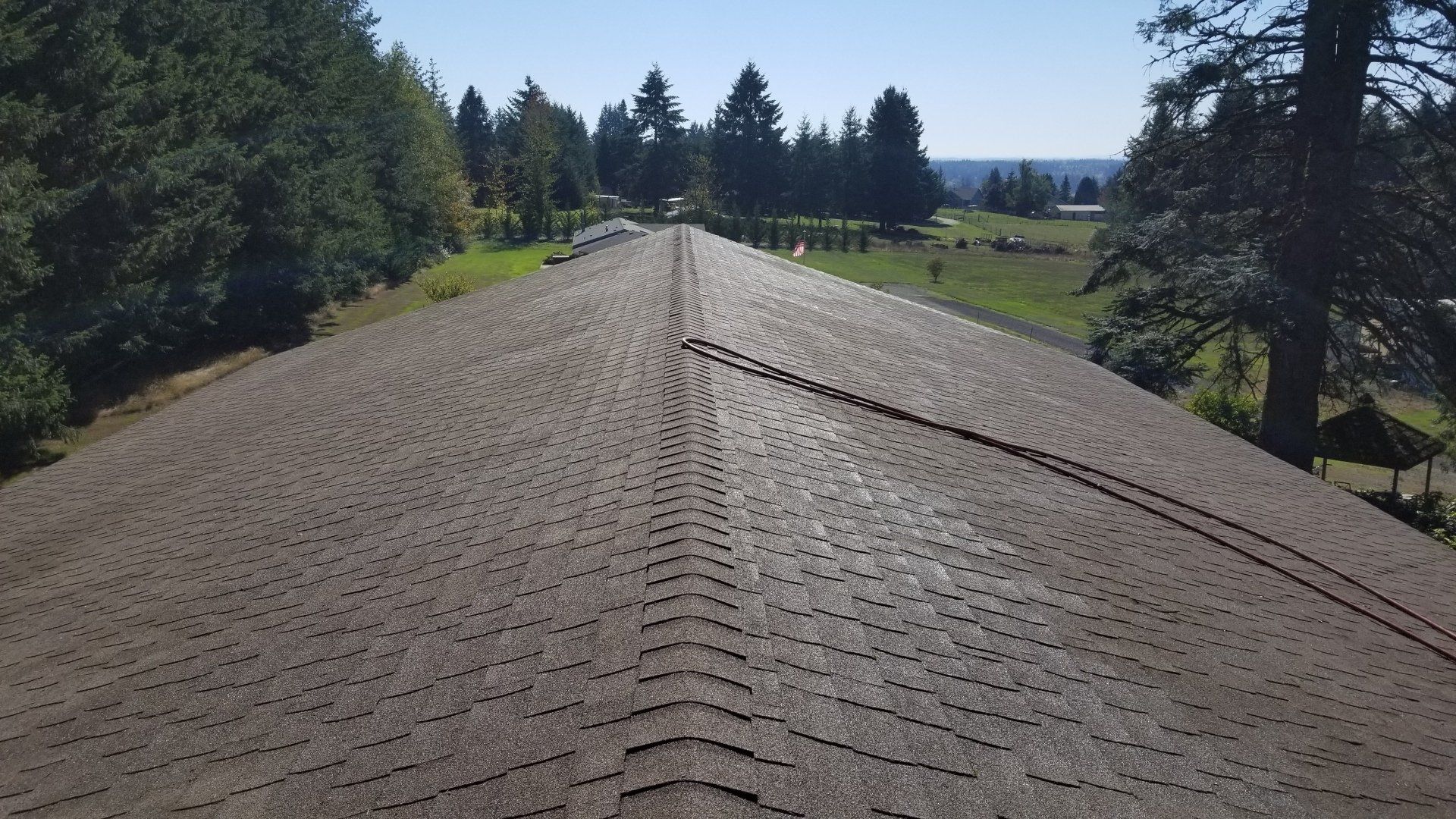 View from roof of house surrounded by green trees and fields on a sunny day.