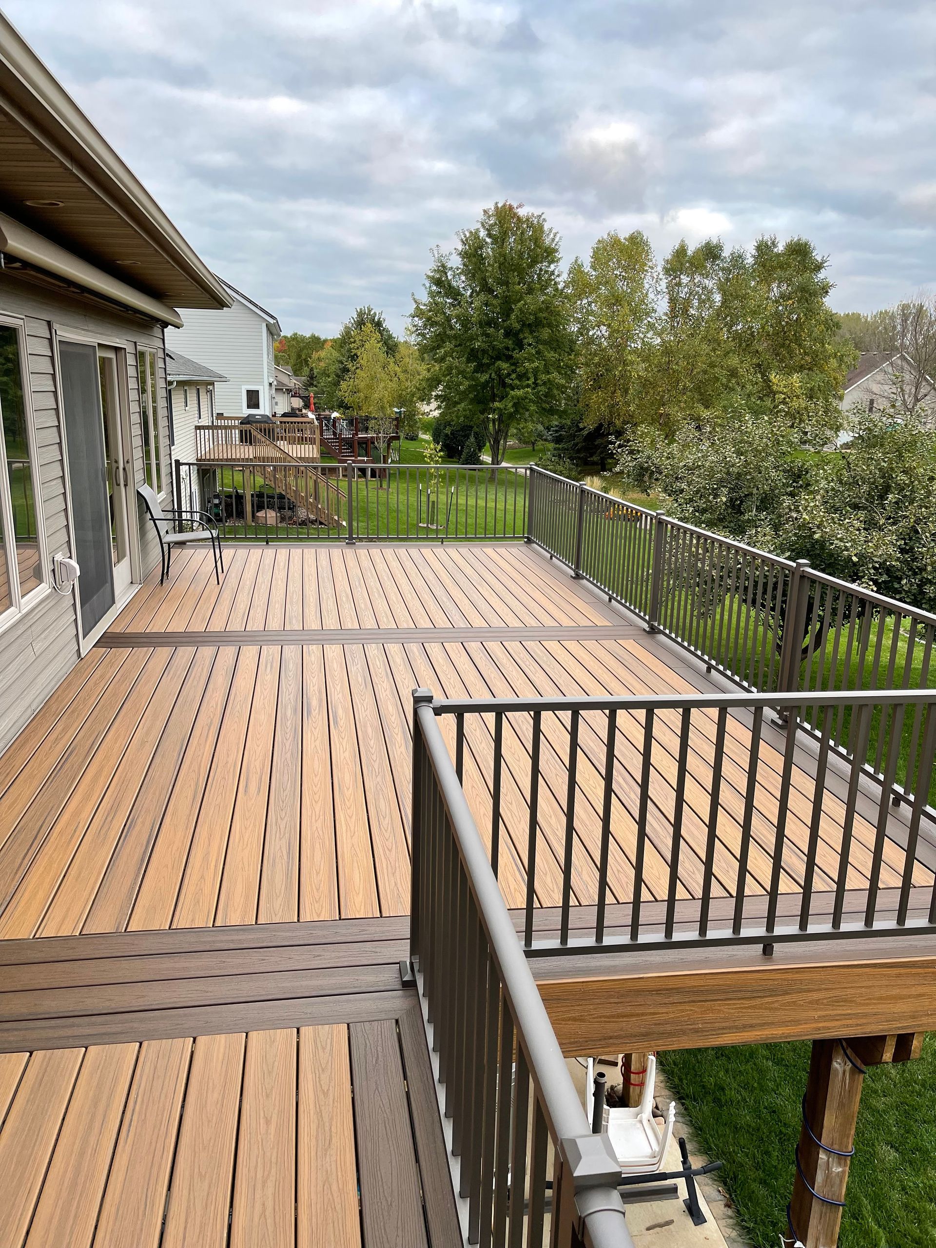 A large wooden deck with a metal railing in front of a house.