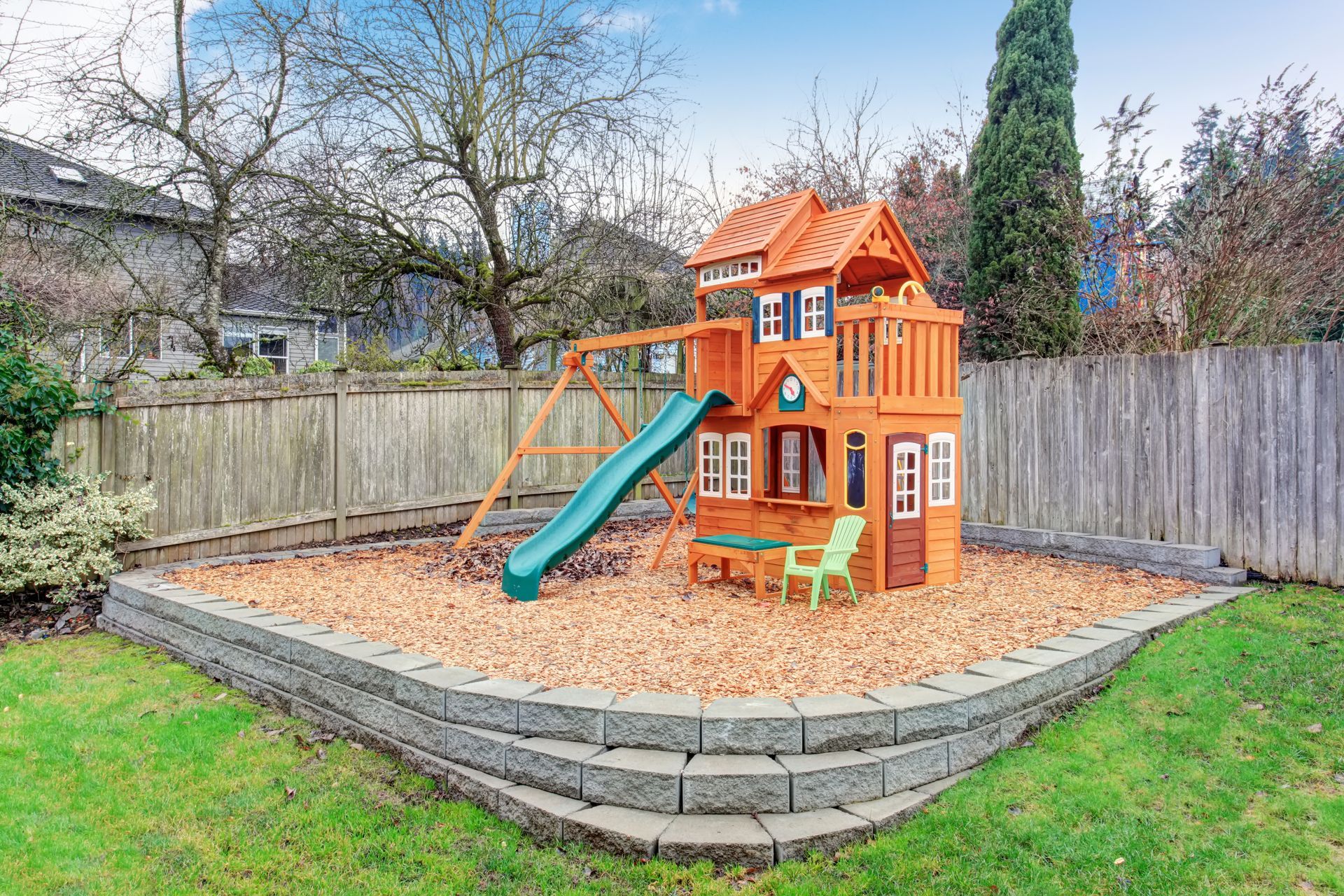 A wooden playhouse with a slide and swings in a backyard.