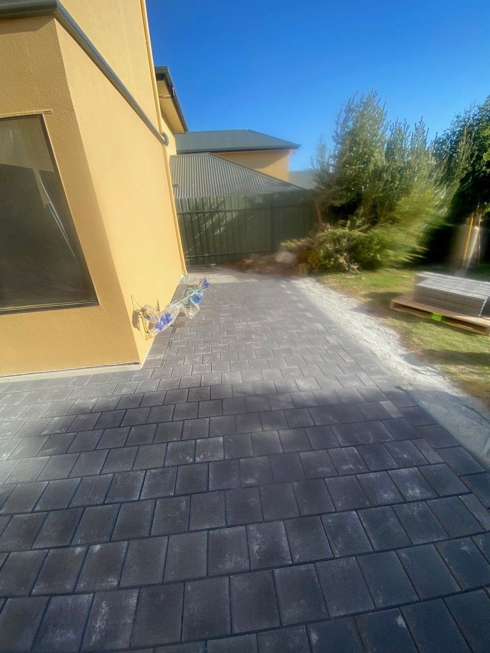 A brick walkway leading to a house with a fence in the background.