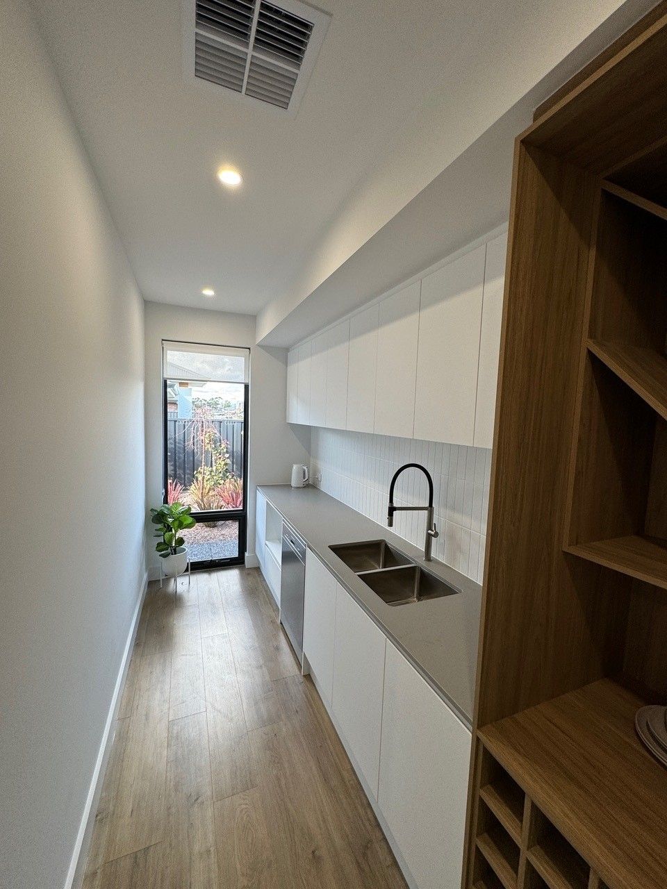 A long hallway leading to a kitchen with white cabinets and a sink.