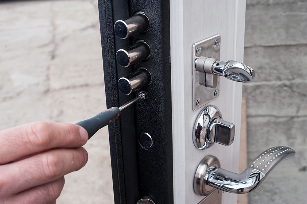 Una persona utilizza un cacciavite sulla serratura di una porta in acciaio con più bulloni, mentre questa è aperta.