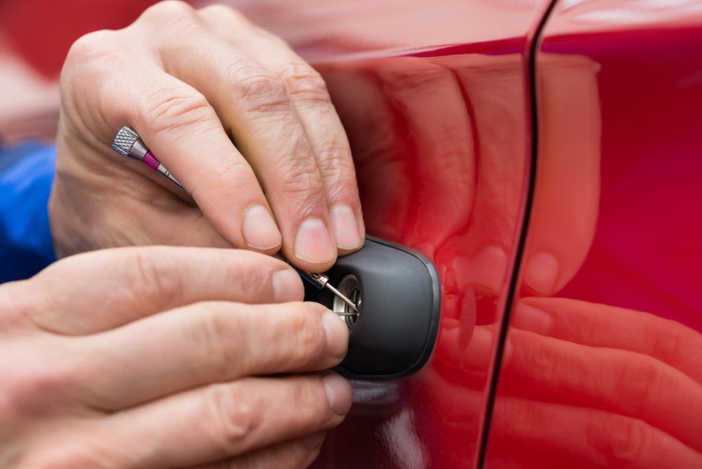 Mani che usano un piccolo strumento per forzare la serratura della portiera di un'auto rossa.