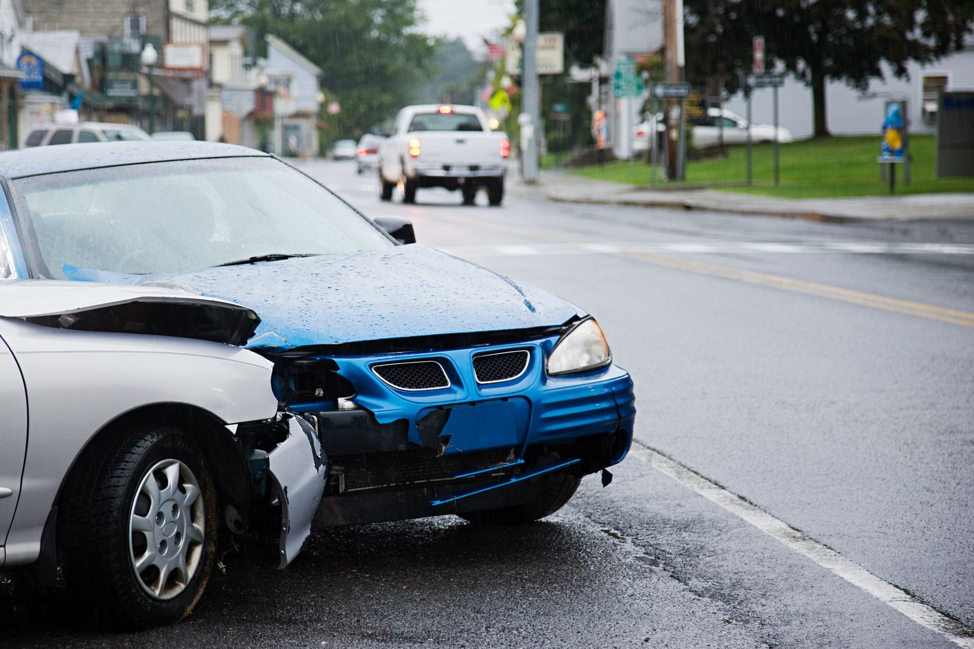 A blue car with a broken bumper is parked on the side of the road