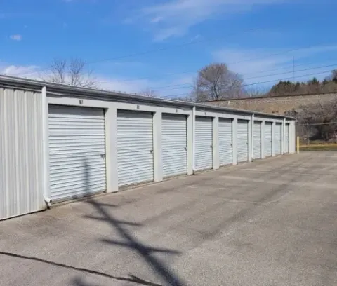 A row of grey storage units with roll-up doors against a blue sky.