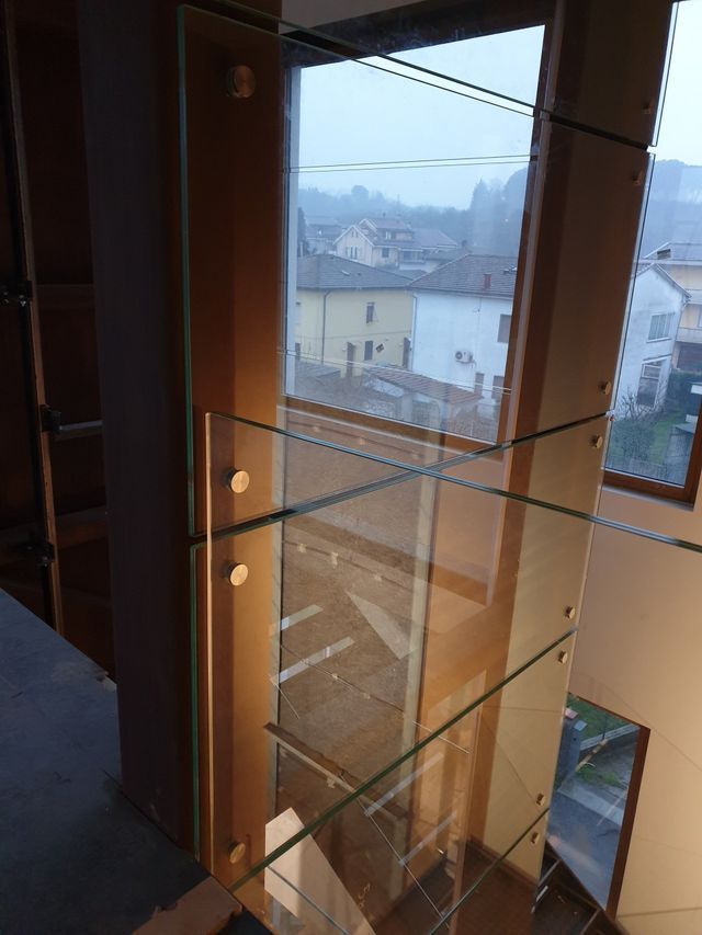 Pannelli di ringhiera in vetro montati con distanziatori metallici circolari su un palo di legno che si affaccia su un quartiere residenziale.