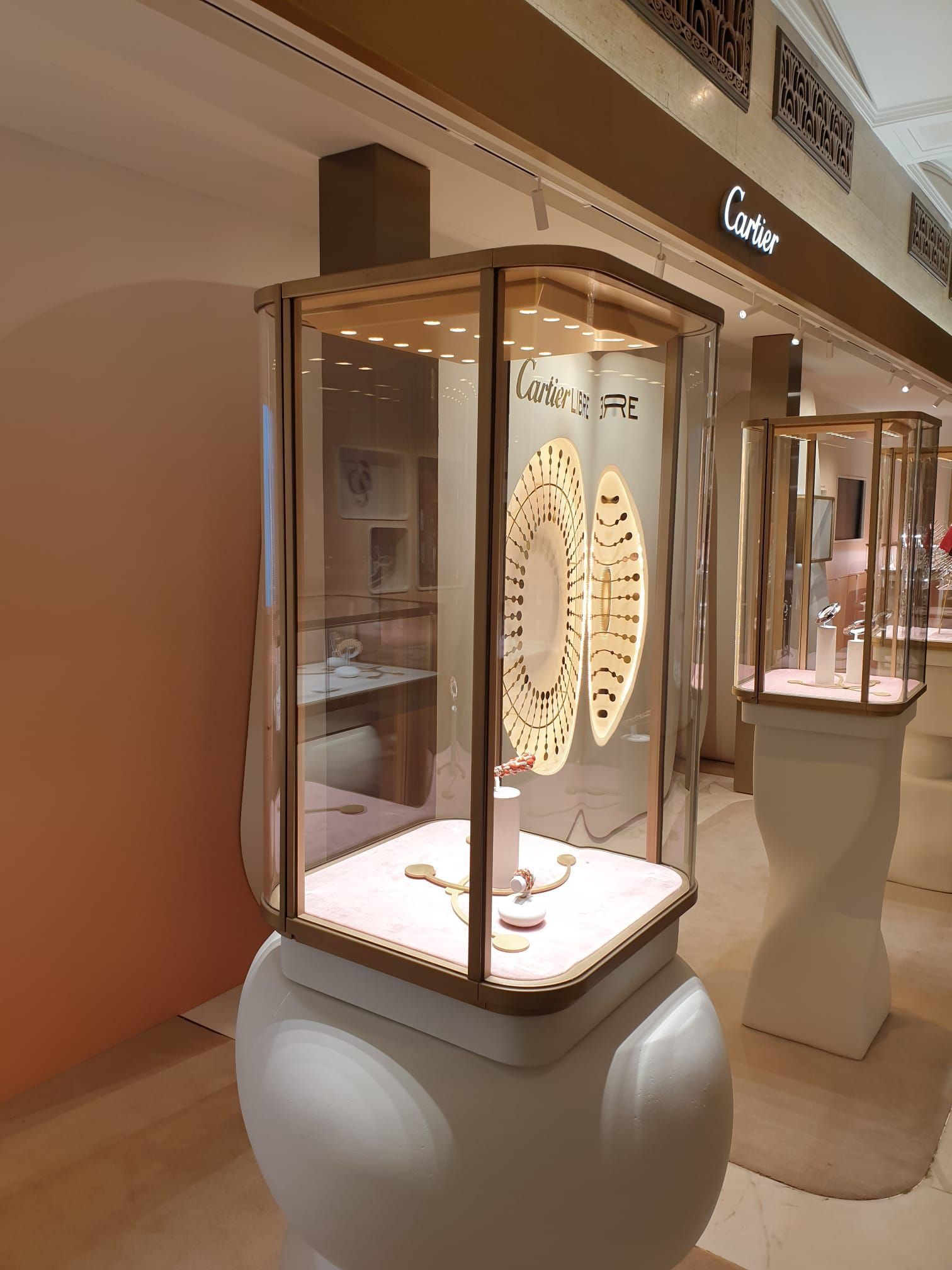 Due vetrine per gioielli Cartier su piedistalli bianchi e arrotondati, all'interno di una boutique ben illuminata.