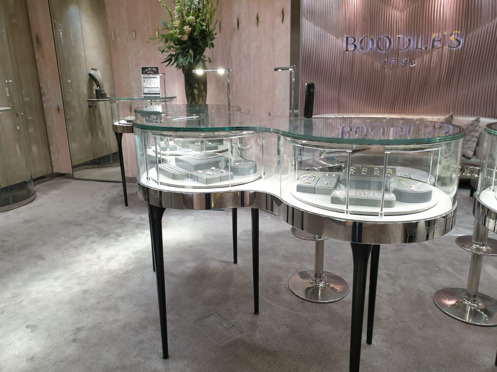 L'interno di un'elegante gioielleria Boodles, caratterizzato da vetrine in vetro curvo su sottili gambe nere e pavimenti lucidi.