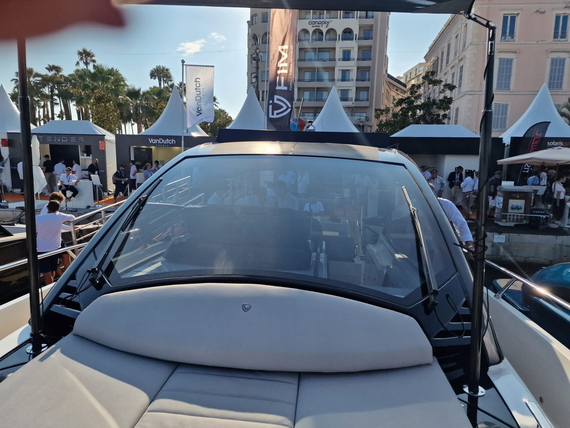 Una vista dal ponte di legno di uno yacht di lusso che si affaccia su un porto pieno di barche e su una città costiera sotto un cielo azzurro.