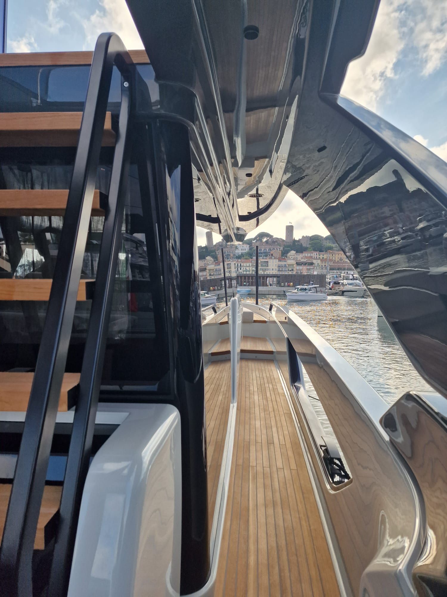 Una lunga finestra rettangolare con tre oblò circolari sul lato dello scafo bianco di uno yacht in un porto turistico.