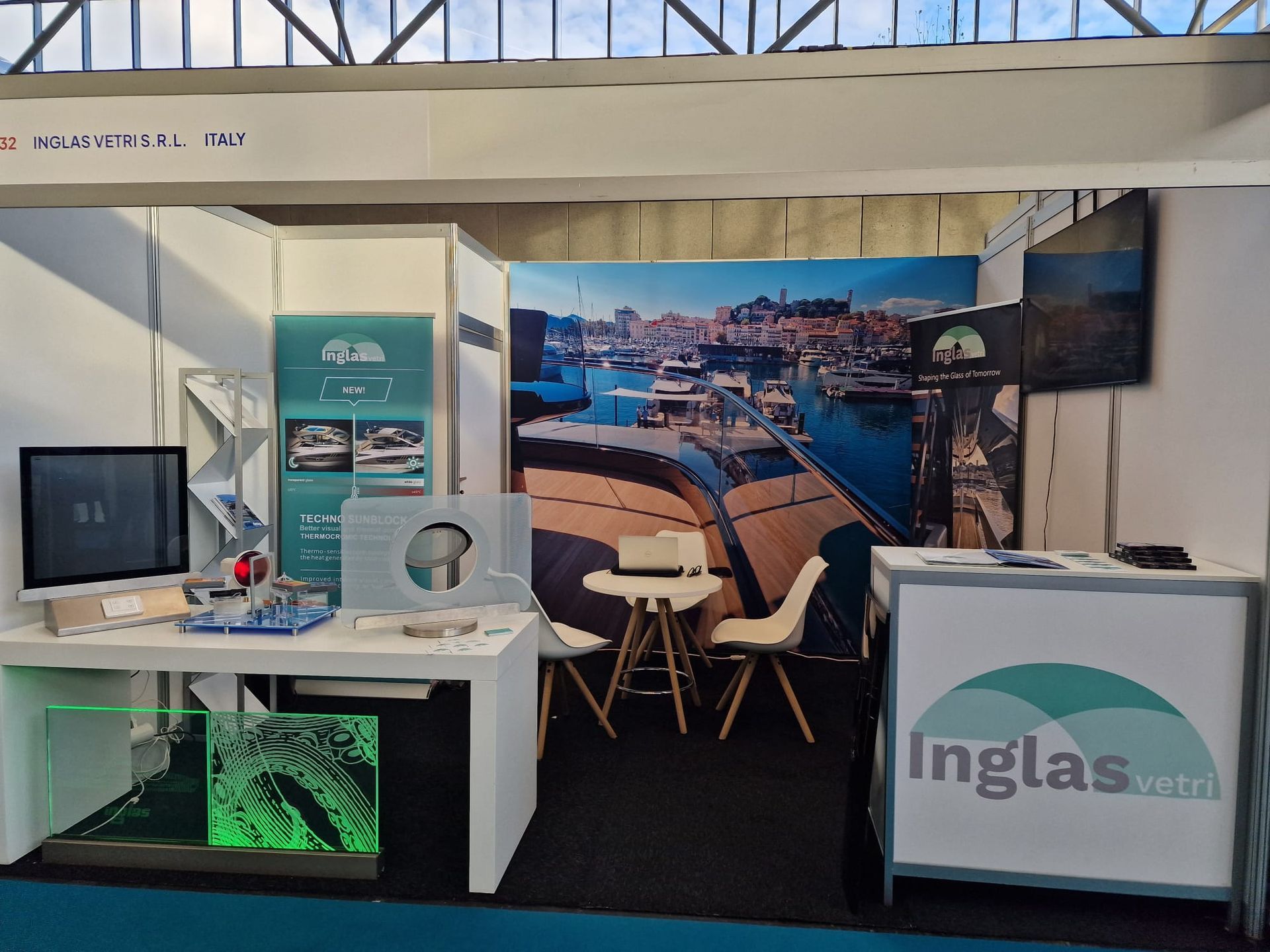 Uno stand fieristico con il logo Inglas, un tavolo con sedie, campioni di prodotto e un grande sfondo raffigurante un porto turistico.