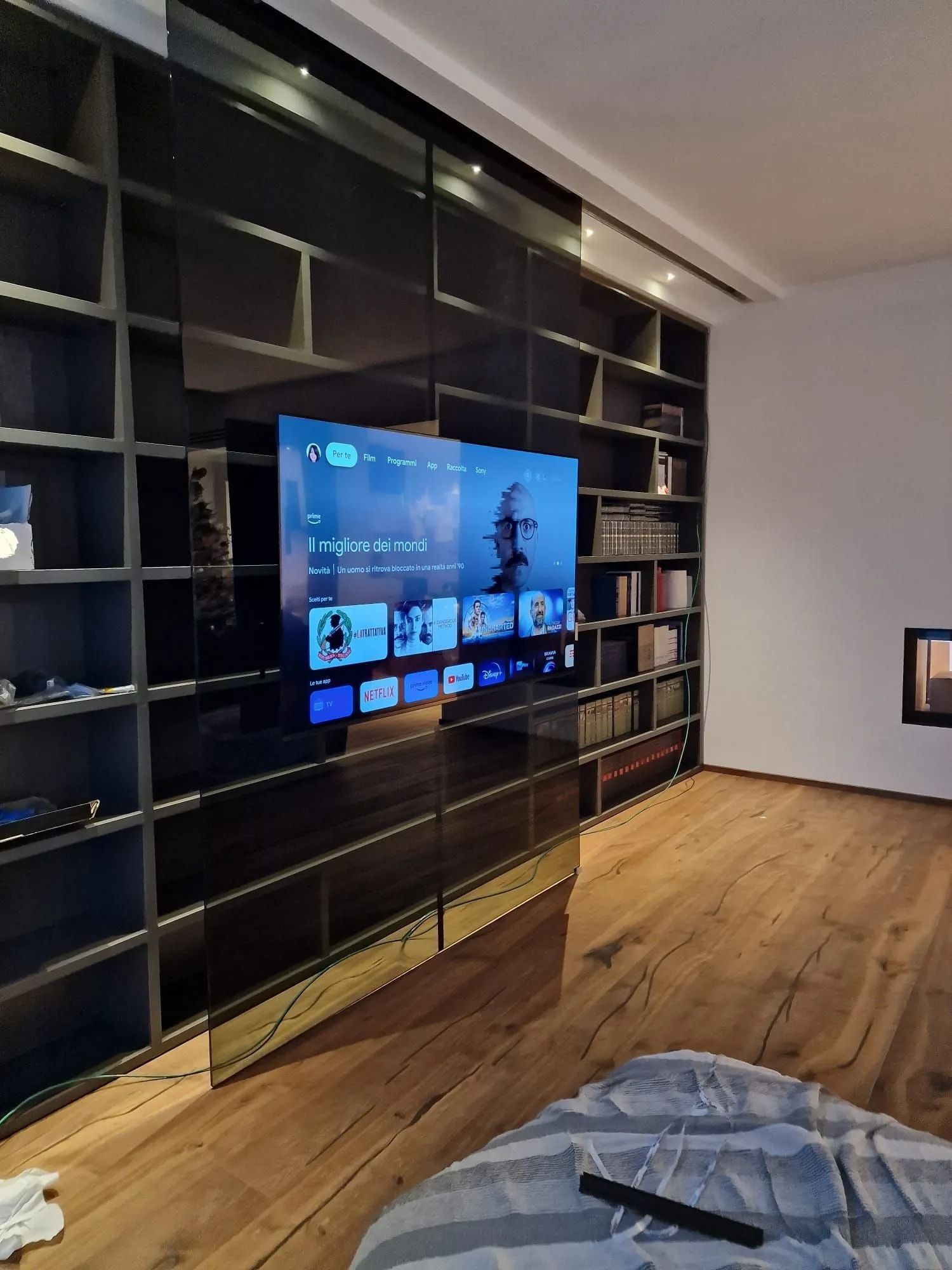 Un televisore a schermo piatto montato su una grande libreria integrata di colore scuro in una stanza con pavimento in legno chiaro.