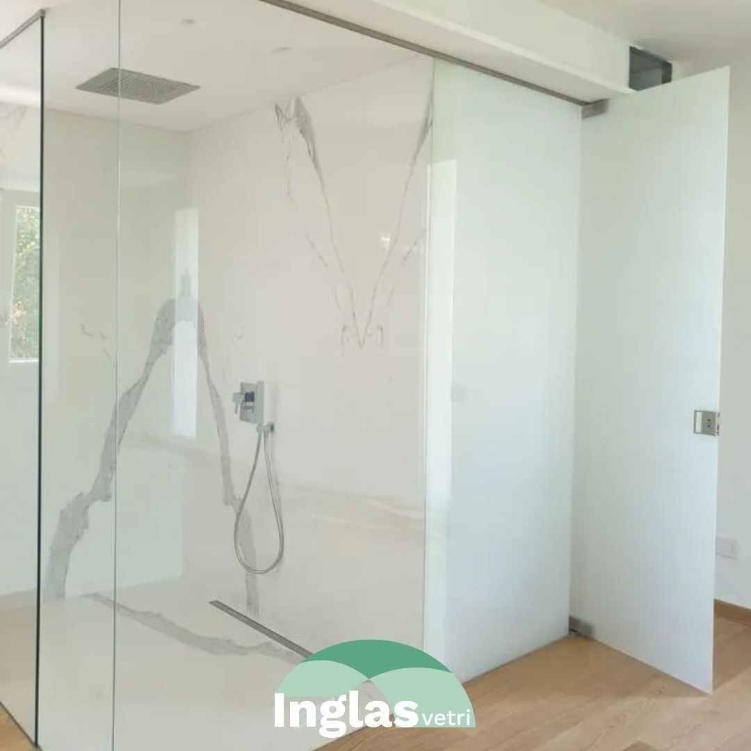 Una cabina doccia in vetro con porta in vetro satinato, pareti rivestite con piastrelle di colore chiaro e soffione a pioggia incassato nel soffitto.