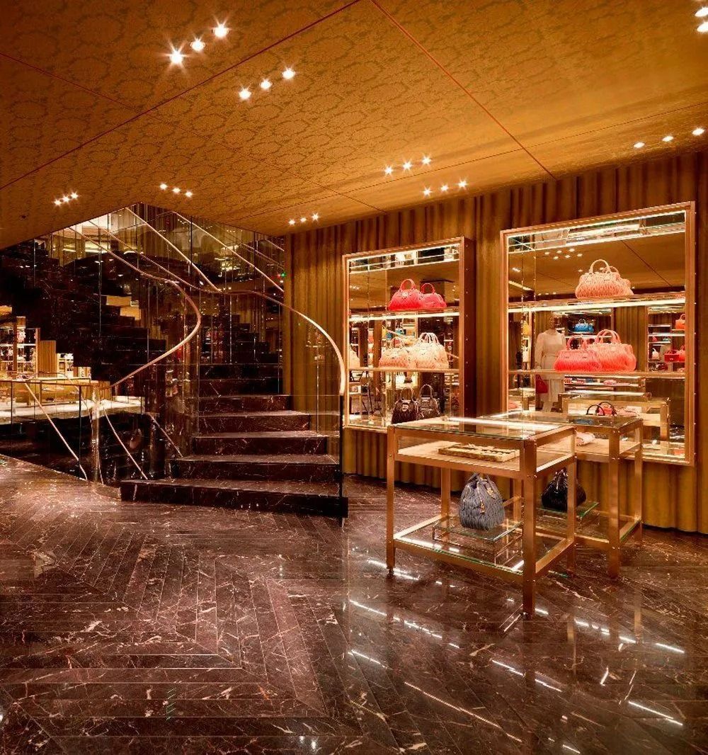 L'interno di una boutique di lusso con pavimenti in marmo, una scala a chiocciola e vetrine piene di borse.