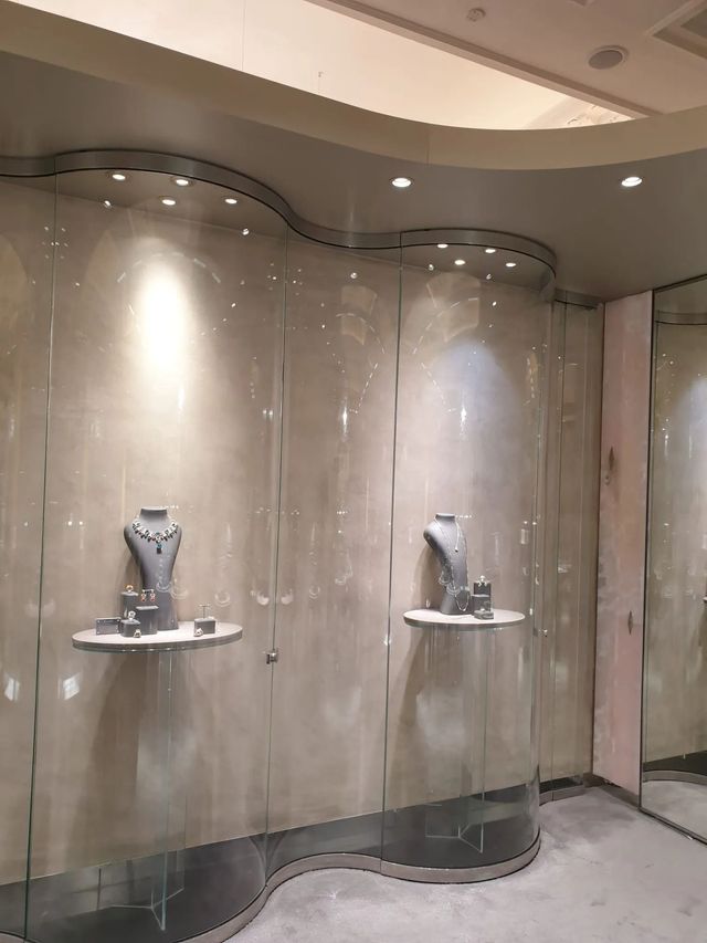 L'allestimento di una gioielleria con due manichini che indossano collane, posizionati su mensole curve contro una parete liscia color beige.