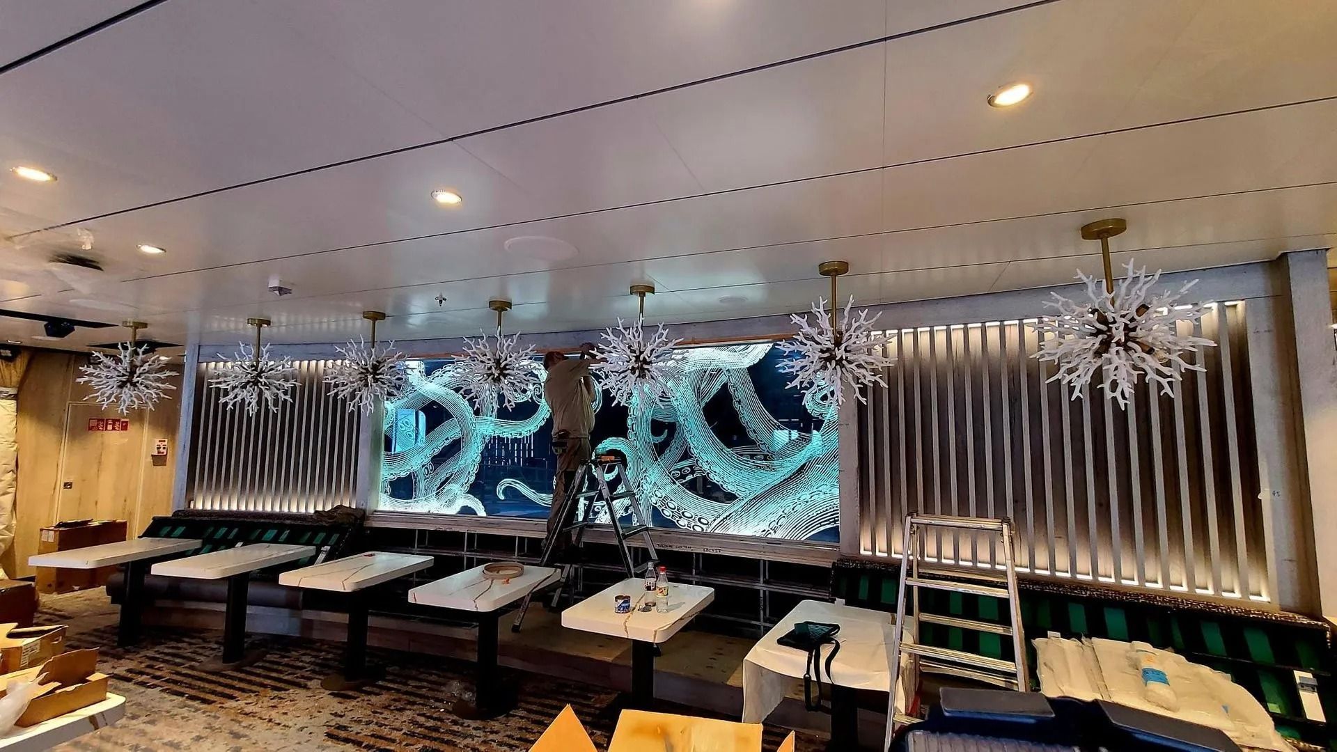 In un'elegante e moderna sala da pranzo, un operaio su una scala si trova di fronte a un grande schermo digitale illuminato raffigurante dei tentacoli.
