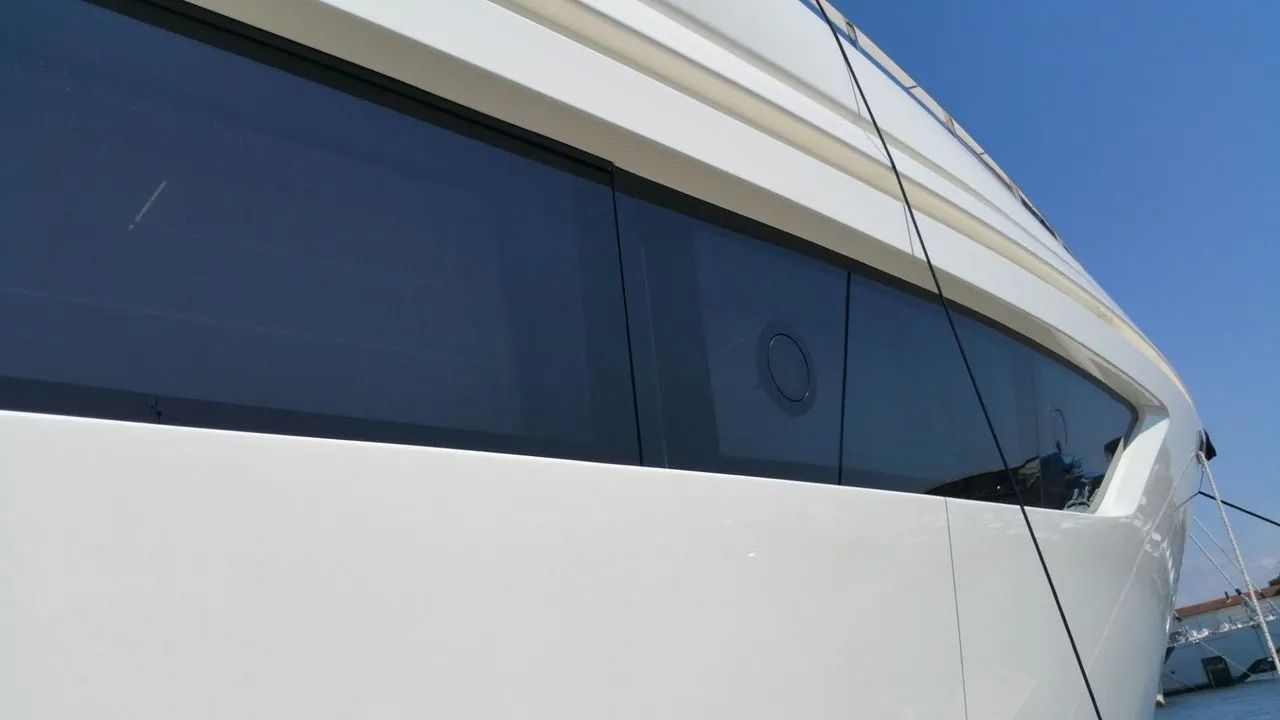 Una vista ravvicinata e angolata dello scafo elegante e bianco di uno yacht, con finestrini scuri e riflettenti che si stagliano contro un cielo azzurro limpido.