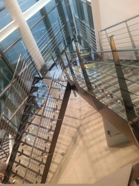 Vista dall'alto di una moderna scala in vetro con ringhiere in metallo all'interno di un luminoso edificio con vetrate a tutta altezza.