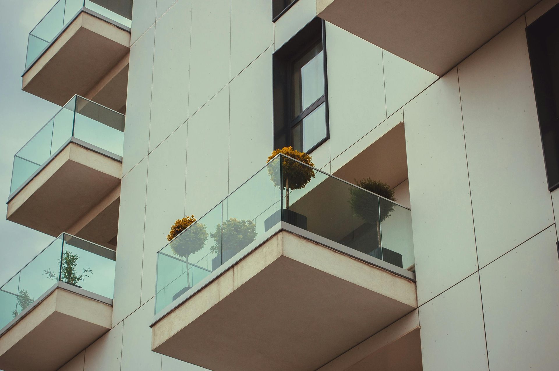 Vista dal basso di un moderno condominio con balconi sovrapposti con ringhiere in vetro e vasi di fiori gialli.